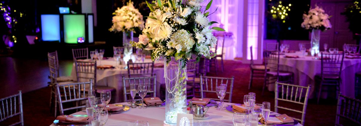 Reception ballroom with a tall white floral centerpiece and purple lighting