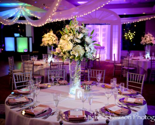 Reception ballroom with a tall white floral centerpiece and purple lighting