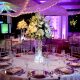 Reception ballroom with a tall white floral centerpiece and purple lighting