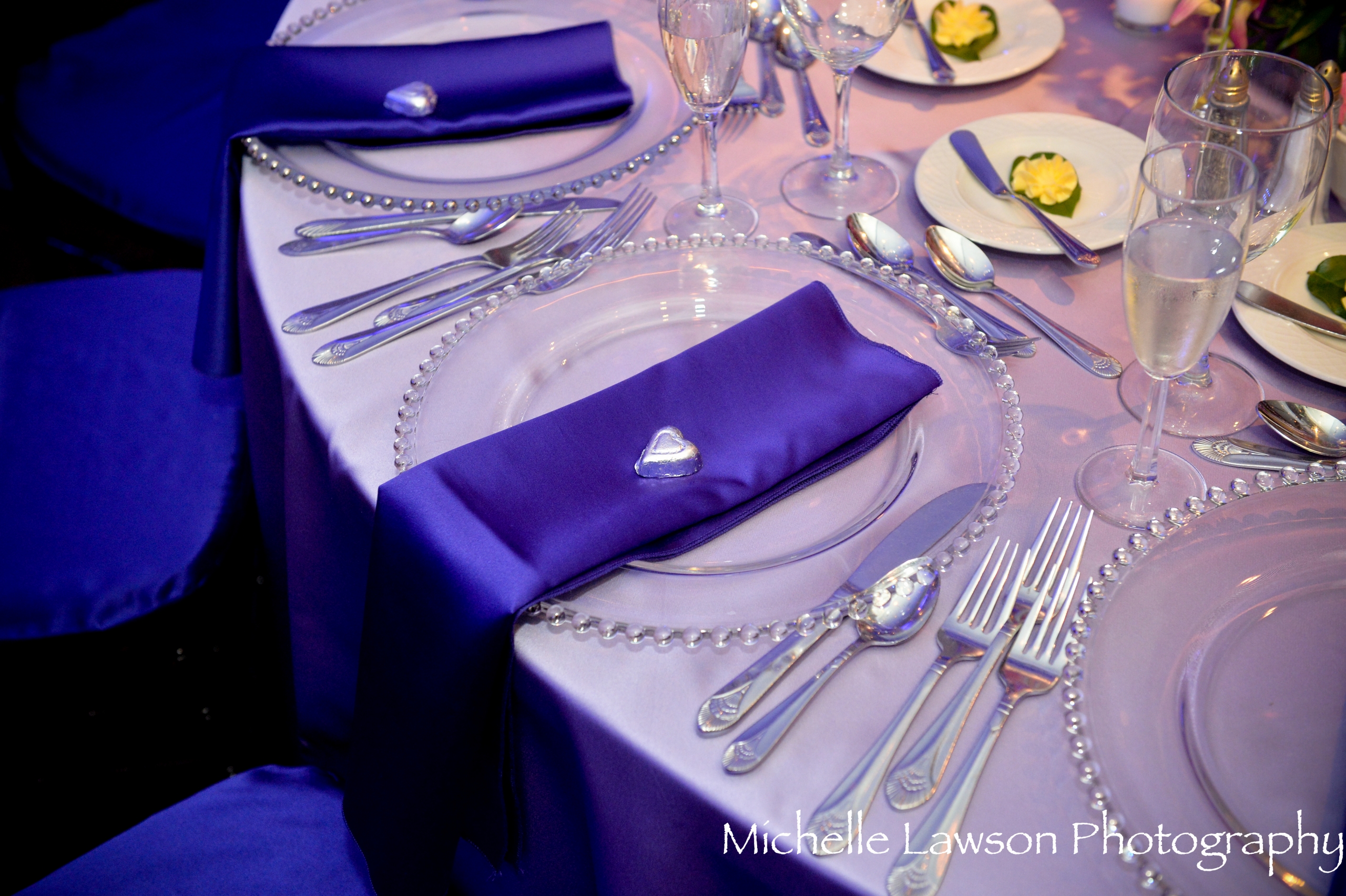 Close-up of an elegant place setting with purple linens and glass charger plates