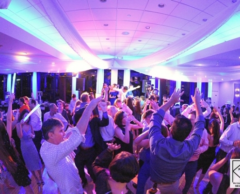 Guests dancing with hands raised on the dance floor under colorful lighting