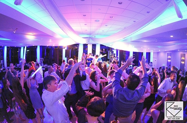 Guests dancing with hands raised on the dance floor under colorful lighting